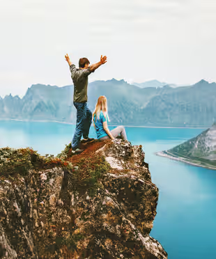 Person standing on a cliff above a coastal landscape.