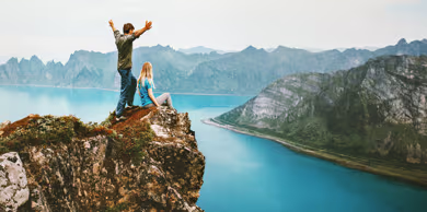 Two people standing on a cliff overlooking a mountain lake.